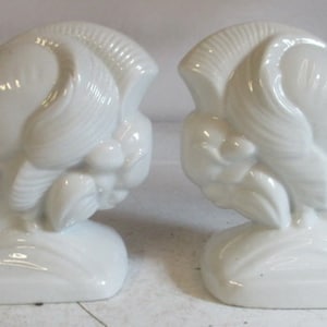 May include: A pair of white ceramic bookends shaped like stylized animal heads, possibly rams or sheep, with their heads bowed down. The bookends are in a classic art deco style.