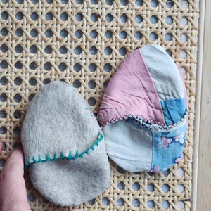 Puede incluir: Dos objetos con forma de huevo cubiertos de tela. Uno es gris con costuras verdes y el otro es rosa, azul y blanco con costuras blancas.