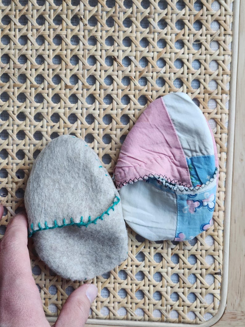 Puede incluir: Dos objetos con forma de huevo cubiertos de tela. Uno es gris con costuras verdes y el otro es rosa, azul y blanco con costuras blancas.