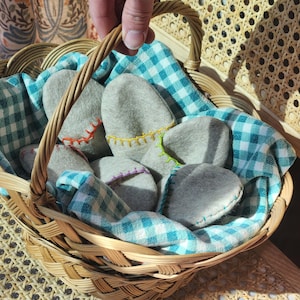 Puede incluir: Una cesta de mimbre llena de pantuflas de fieltro gris, forrada con un pa&ntilde;o a cuadros azul y blanco. La cesta tiene un asa y est&aacute; sentada sobre una superficie tejida.