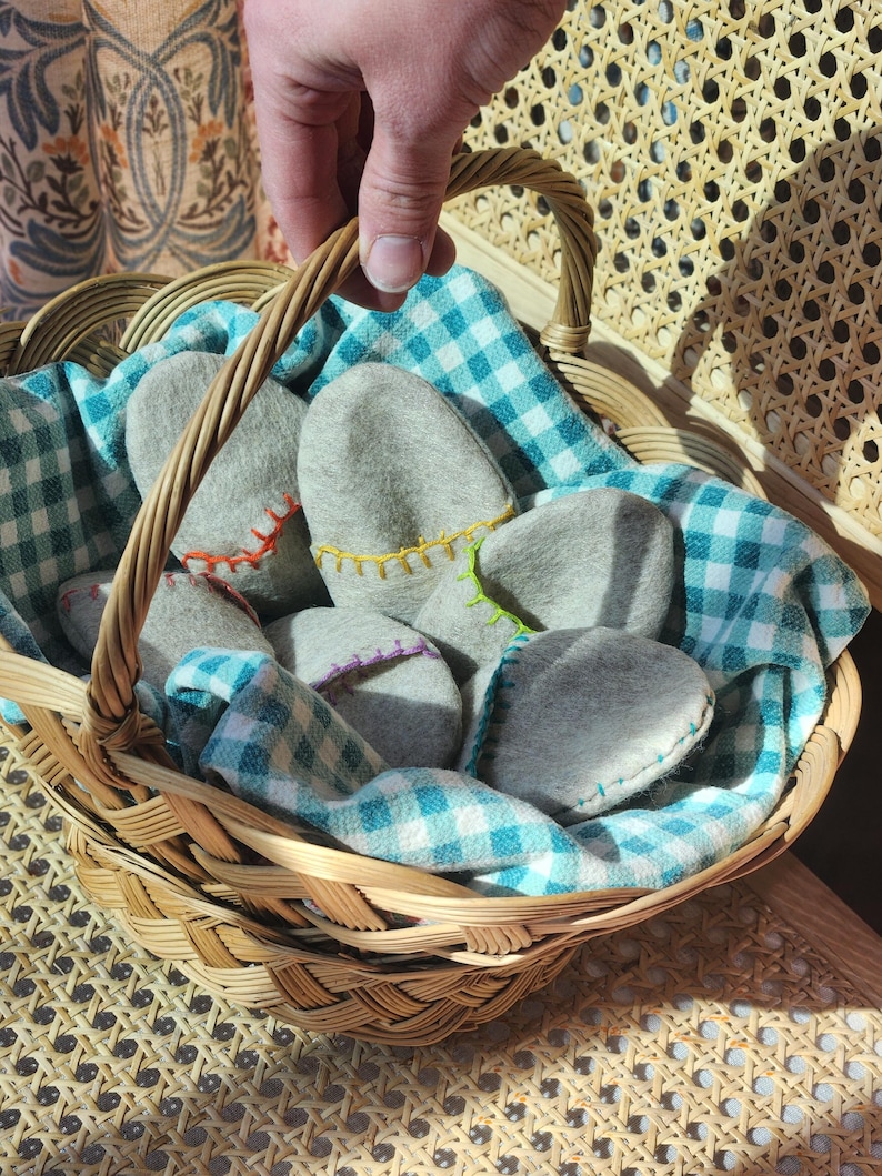 Puede incluir: Una cesta de mimbre llena de pantuflas de fieltro gris, forrada con un pa&ntilde;o a cuadros azul y blanco. La cesta tiene un asa y est&aacute; sentada sobre una superficie tejida.