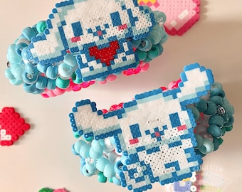 Könnte beinhalten: Zwei bunte Perlenarmbänder mit pixelartigen weißen Hundedesigns. Die Armbänder sind aus blauen, rosa und türkisfarbenen Perlen gefertigt.
