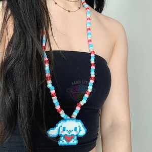 May include: A colorful beaded necklace with a pixelated dog charm. The necklace is made of red, blue, and pink beads. The charm is white with a red heart.