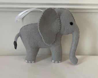 May include: A gray felt elephant ornament with a white string for hanging. The elephant has a black eye and a small tail.