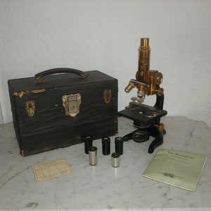 May include: Antique brass microscope with a black leather carrying case, four small metal containers, and a booklet titled "The Microscope".