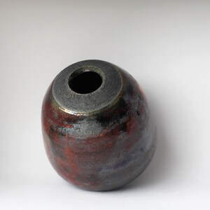 May include: A small, round, ceramic vase with a dark grey glaze and a red and blue iridescent finish.