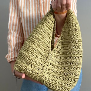 May include: A green crocheted tote bag with a wide, open top and a single strap. The bag is made of a lightweight, open weave material.