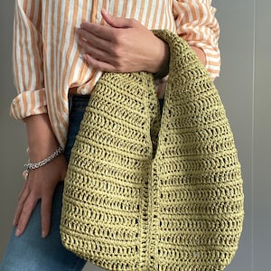 May include: A green crocheted tote bag with a slouchy design. The bag is made of a lightweight, open weave material.
