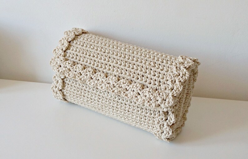 May include: A beige crocheted clutch bag with a scalloped edge.