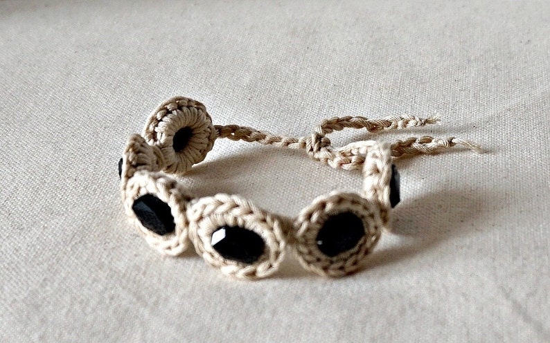 May include: A crocheted bracelet with black beads. The bracelet is made of a natural beige colored string.