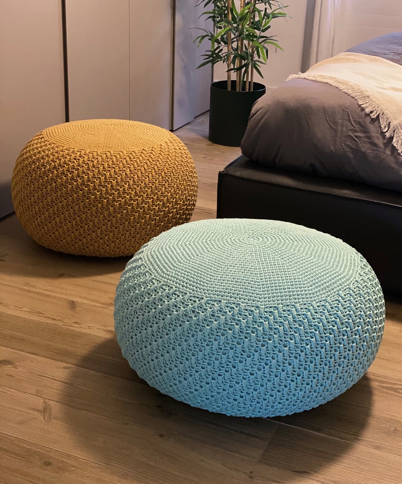May include: Two round knitted ottomans, one mustard yellow and one light blue, on a wooden floor.
