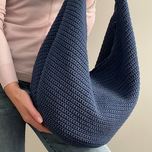 May include: A large, dark blue crocheted tote bag with a slouchy, unstructured design. The bag is made with a simple stitch pattern and has a wide, open top.