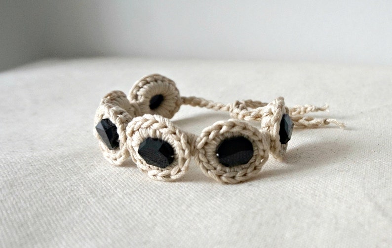 May include: A crocheted bracelet with black gemstone beads. The bracelet is made with cream-colored yarn and has a simple design.