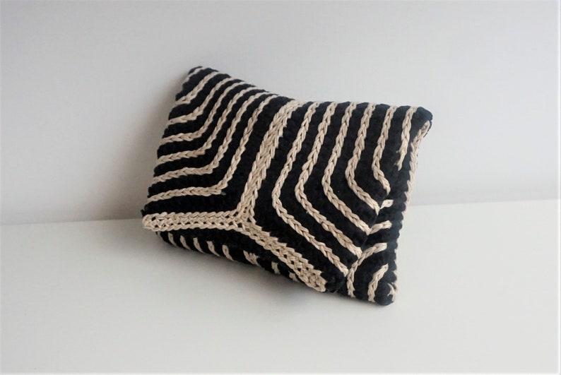 Puede incluir: Una almohada a rayas negras y beige con un patr&oacute;n geom&eacute;trico. La almohada est&aacute; hecha de un tejido tejido y tiene una superficie suave y texturizada.