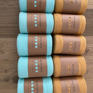 May include: Ten spools of yarn, five are light blue and five are mustard yellow. Each spool has a brown label with the text "PAINTBOX YARNS" and "RECYCLED RIBBON".