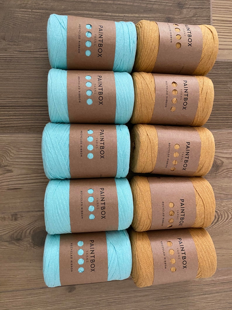 May include: Ten spools of yarn, five are light blue and five are mustard yellow. Each spool has a brown label with the text "PAINTBOX YARNS" and "RECYCLED RIBBON".
