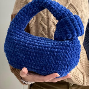 Op de afbeelding: Een blauwe gehaakte handtas met een geknoopte handvat.
