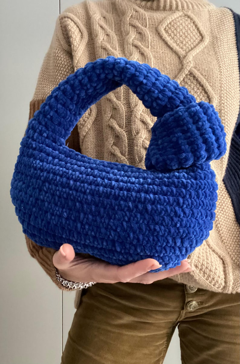 Op de afbeelding: Een blauwe gehaakte handtas met een geknoopte handvat.