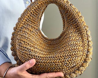 May include: A crescent-shaped handbag crafted from a textured, braided cord in shades of metallic gold and muted grey. The bag features a continuous, thick, rounded border edge and a singular integrated handle opening at the top centre.