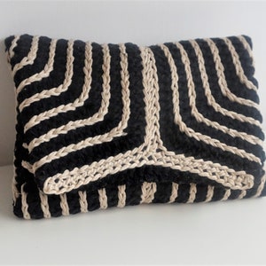 Puede incluir: Un embrague tejido negro y beige con un patr&oacute;n geom&eacute;trico. El embrague est&aacute; hecho de una tela suave y texturizada y tiene un dise&ntilde;o simple y elegante.