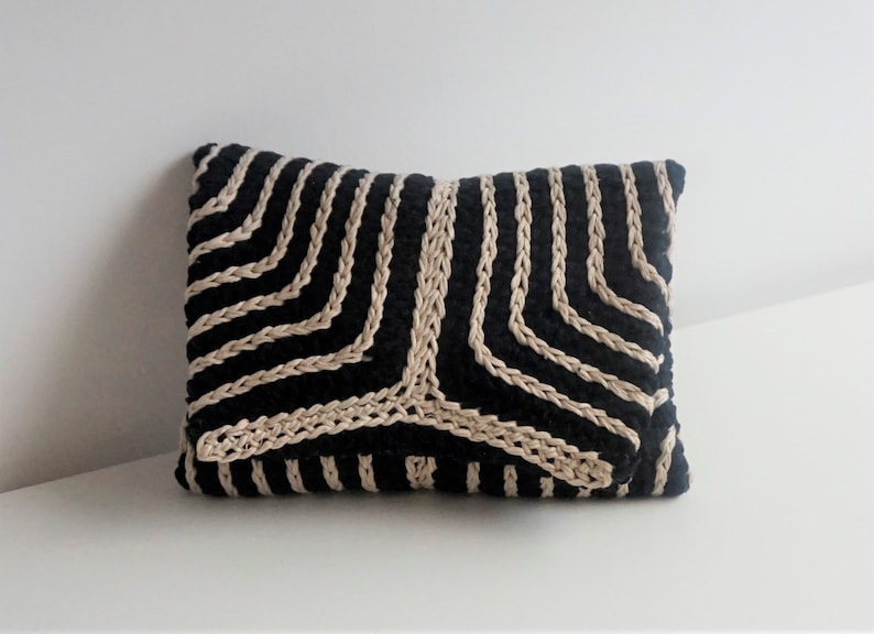 Puede incluir: Almohada rayada en negro y beige con un patr&oacute;n geom&eacute;trico. La almohada est&aacute; hecha de un tejido tejido y tiene una forma rectangular.