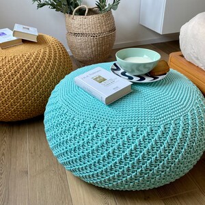 May include: Two round knitted ottomans, one mustard yellow and one light blue, with a book and a bowl on top of the blue ottoman.