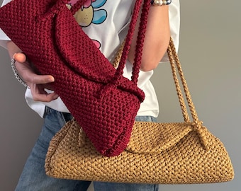 May include: Two rectangular crochet shoulder bags, one in deep burgundy and one in tan, each featuring a textured woven pattern, a fold-over flap closure, and two matching braided shoulder straps attached to the top of the bag.