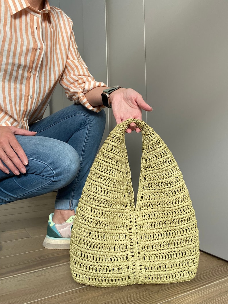 May include: A light green crocheted tote bag with a wide, open top and a single handle.