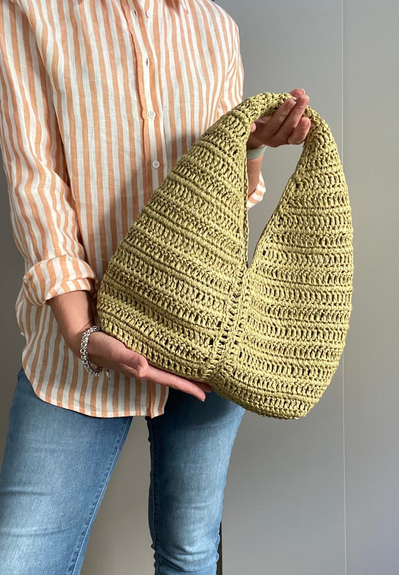 May include: A light green crocheted tote bag with a triangular shape. The bag has a wide opening and a single strap.