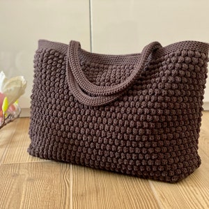 May include: A brown crocheted tote bag with a textured, bumpy design. The bag has two handles.