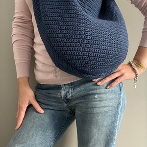May include: A dark blue crocheted bag worn over the shoulder of a person wearing a pink long-sleeved shirt and blue jeans.