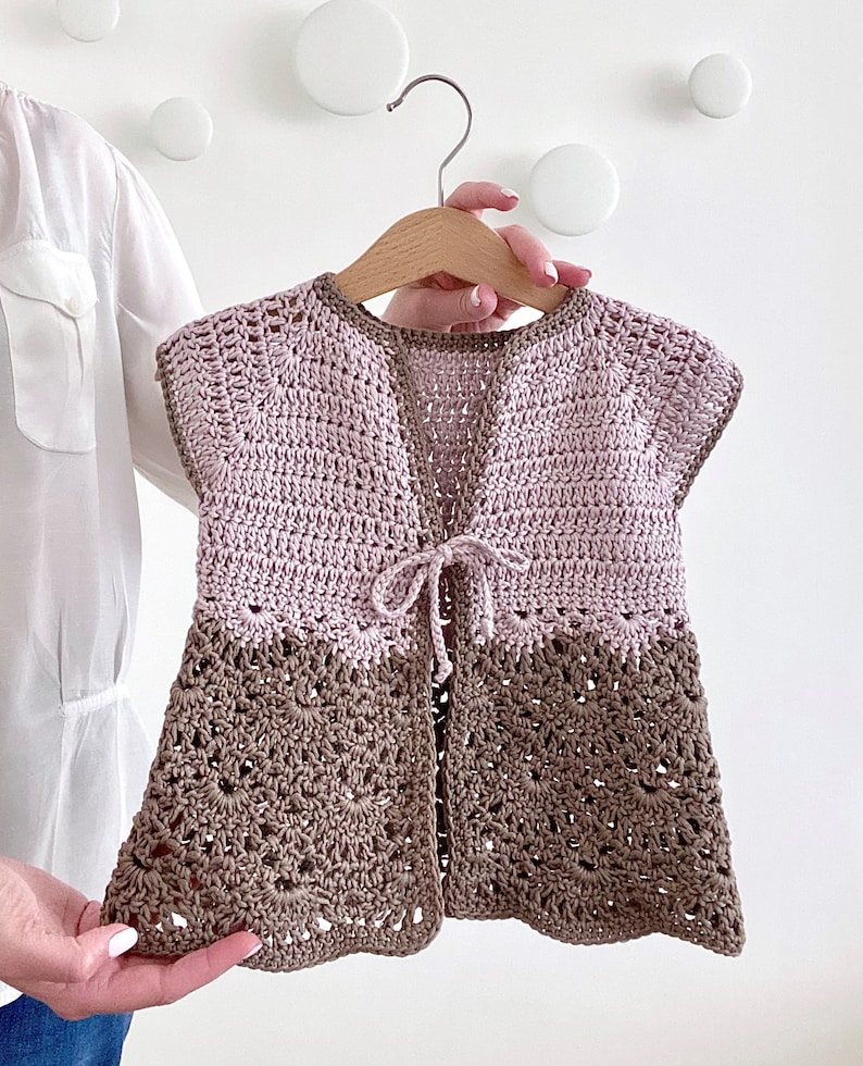 Op de afbeelding: Een gehaakt babyvest in roze en bruin. Het vest heeft een strik aan de voorkant en korte mouwen.