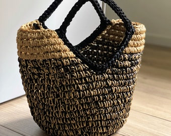 May include: A black and tan crocheted tote bag with two handles. The bag is made of a thick, woven material and has a rounded shape.