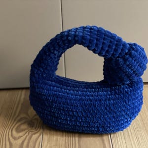 Op de afbeelding: Een klein, blauw, gehaakt handtasje met een geknoopte handvat.