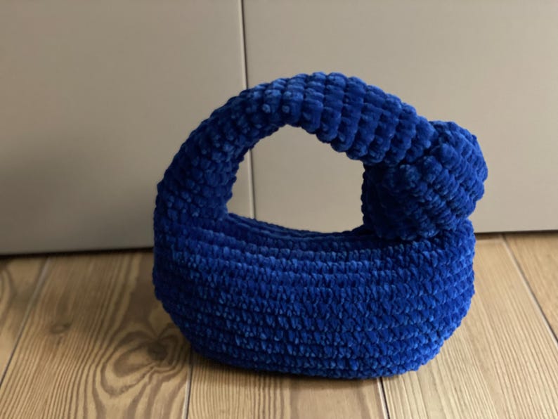 Op de afbeelding: Een klein, blauw, gehaakt handtasje met een geknoopte handvat.