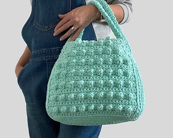 May include: A light green crocheted tote bag with a textured, bumpy design. The bag has two handles and is large enough to carry everyday essentials.