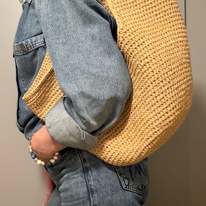 May include: A large, woven, light-yellow tote bag with a matching clutch. The bag has a rectangular shape with a wide strap. The texture of the bag appears to be made of a thick, natural fibre. The bag is carried over the shoulder.