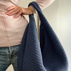May include: A dark blue crocheted tote bag with a long strap. The bag is large and roomy, and would be perfect for carrying everyday essentials.