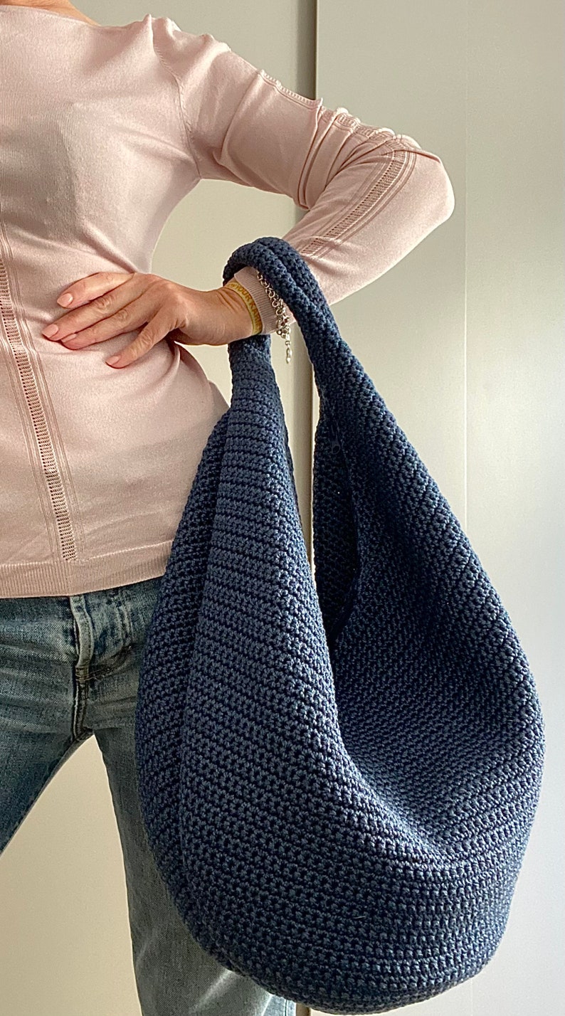 May include: A dark blue crocheted tote bag with a long strap. The bag is large and roomy, and would be perfect for carrying everyday essentials.