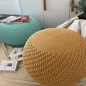 May include: Two crocheted ottomans, one in a light blue color and the other in a mustard yellow color. Both ottomans have a textured, woven design.