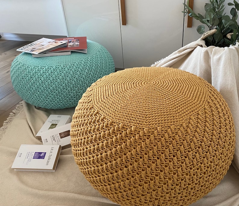 May include: Two crocheted ottomans, one in a light blue color and the other in a mustard yellow color. Both ottomans have a textured, woven design.