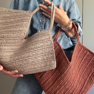 Peut inclure: Deux sacs fourre-tout crochetés à la main. L'un est de couleur beige clair, l'autre est rouge-orangé. Les deux sacs ont une forme rectangulaire avec une large ouverture et de longues anses. Les sacs sont faits d'un fil épais et texturé.