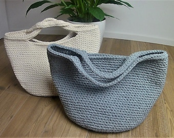 May include: Two crocheted tote bags, one in a light beige colour and the other in a light blue colour. Both bags have a wide, rounded bottom and two long handles.