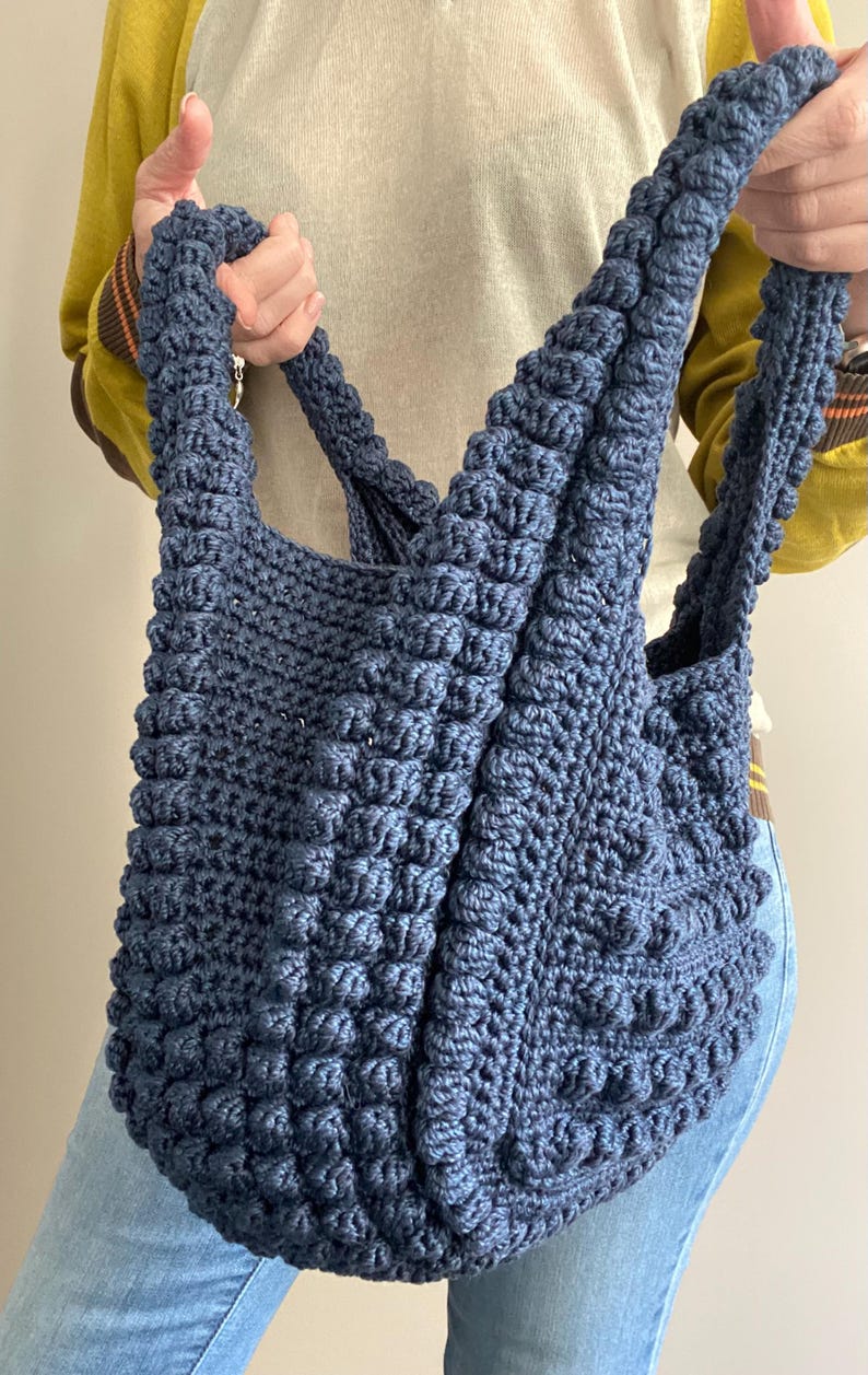 May include: A large, blue crocheted tote bag with a textured, puffy design. The bag has two long straps.