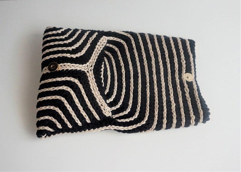 Puede incluir: Clutch de crochet a rayas negras y crema con cierres de presi&oacute;n dorados.