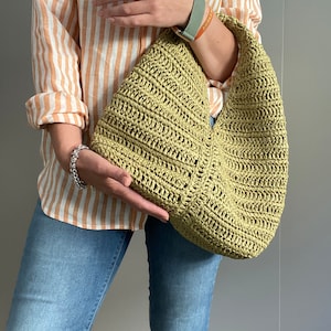 May include: A light green crocheted tote bag with a wide, curved opening. The bag is made of a thick, textured yarn and has a casual, relaxed style.