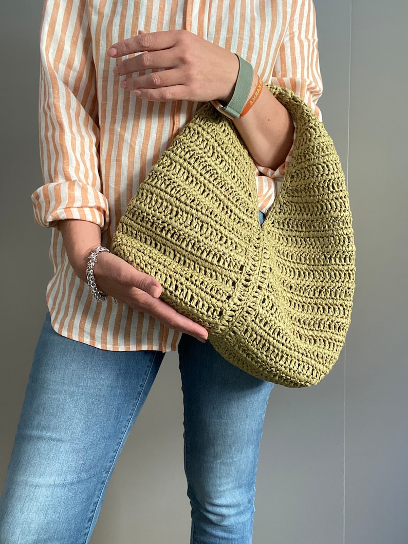 May include: A light green crocheted tote bag with a wide, curved opening. The bag is made of a thick, textured yarn and has a casual, relaxed style.
