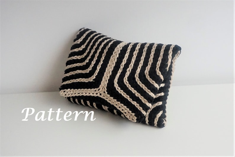 Puede incluir: Una almohada a rayas negras y beige con un patr&oacute;n geom&eacute;trico. La almohada est&aacute; hecha de un tejido tejido y tiene una superficie suave y texturizada.