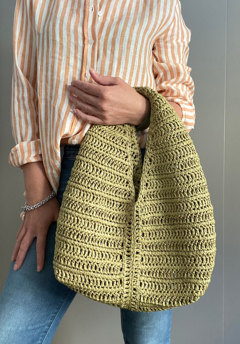 May include: A green crocheted tote bag with a slouchy design. The bag is made of a lightweight, open weave material.