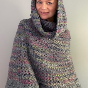 Puede incluir: Un poncho con capucha confeccionado con hilo jaspeado que presenta una mezcla de tonos grises, azules, rosas y amarillos. La prenda tiene un patrón de punto de ganchillo texturizado, un cuello amplio y una silueta holgada.